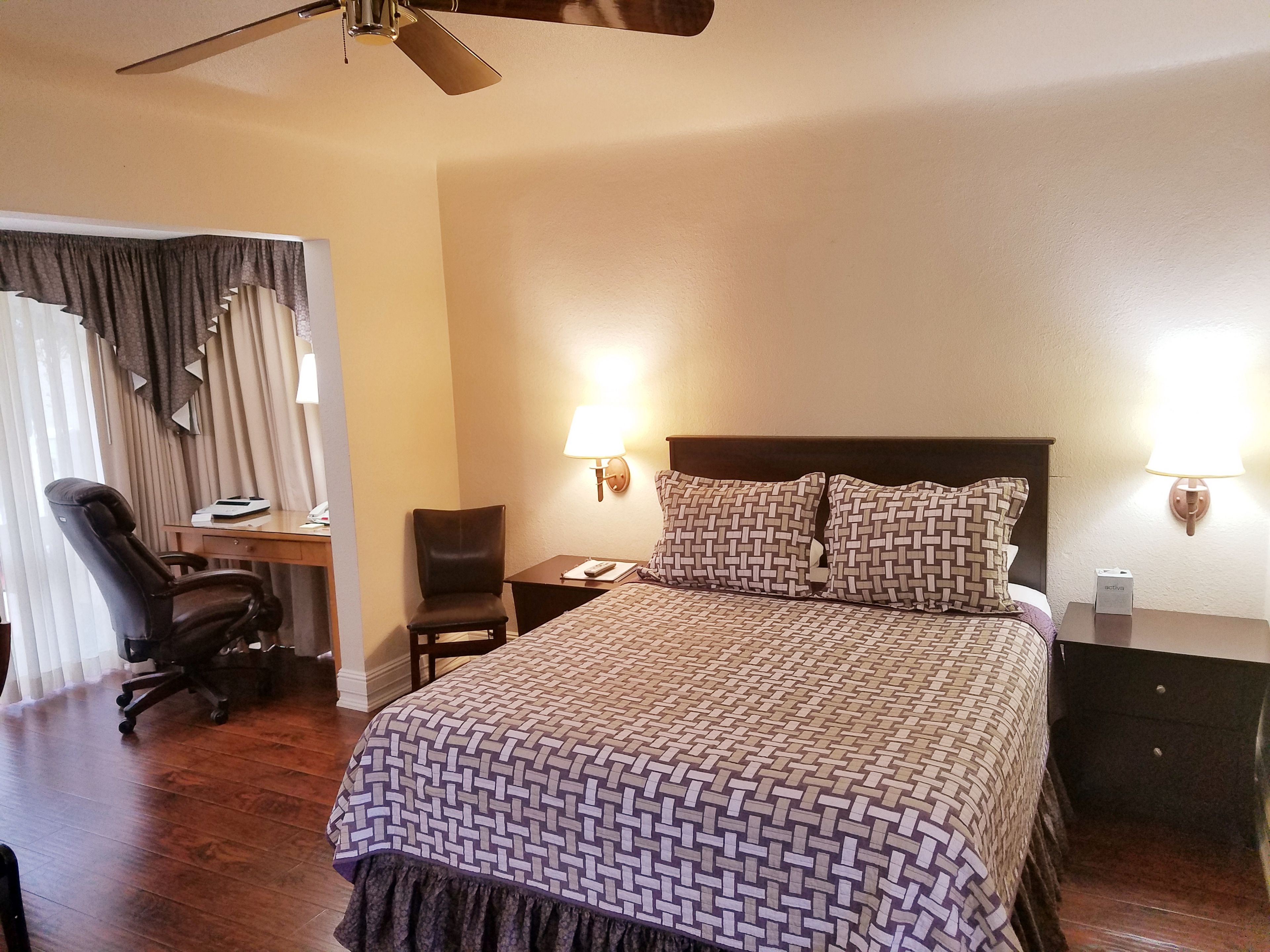 A hotel room with a bed, desk, chair, and two wall-mounted lamps.