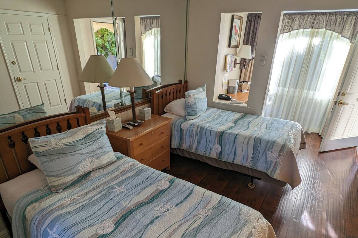 Ein Schlafzimmer mit zwei Betten, Holz-Kopfteilen, einem Deckenventilator und einem Fenster mit Vorhängen.