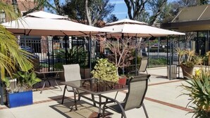 An outdoor patio area with tables and chairs under umbrellas, surrounded by potted plants and trees. - Los Gatos Garden Inn Hotel (Los Gatos)