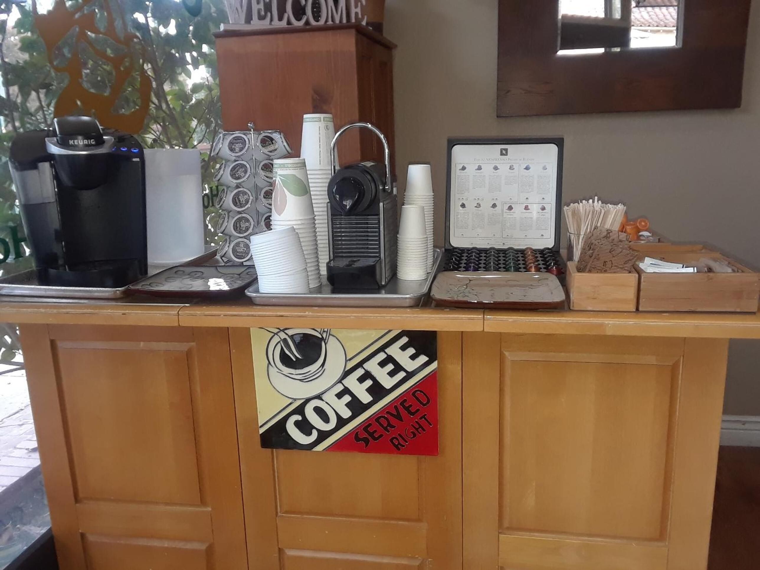 Estação de café com máquina Keurig, copos descartáveis e cardápio de café.