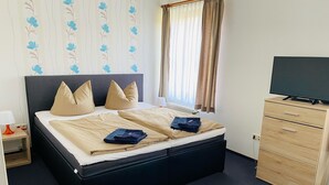 Ein Hotelzimmer mit einem Bett, einem Fernseher, einer Holzkommode und einem Fenster mit Vorhängen.