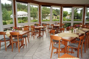 Un restaurant doté de nombreuses tables et chaises, de grandes fenêtres et offrant une vue sur la verdure environnante.