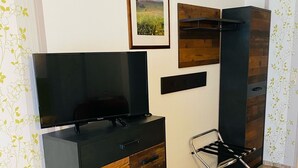 Ein modernes Zimmer mit Fernseher, Holzschrank, Metallstuhl und einem gerahmten Bild an der Wand.