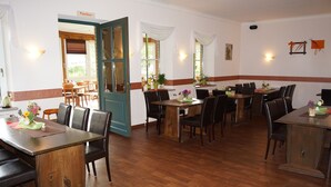 Ein Restaurant mit Holztischen und -stühlen, einer blauen Tür und einer weißen Wand mit rotem Streifen.