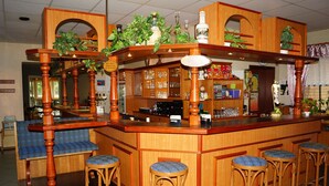 Eine Bar mit Holzhockern, einer Theke und Regalen mit Flaschen und Gläsern.