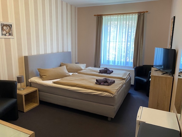 Ein Hotelzimmer mit Bett, Schreibtisch, Stuhl, Fernseher und einem Fenster mit Vorhängen.
