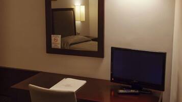 Ein Hotelzimmer mit Schreibtisch, Stuhl, Fernseher, Spiegel und einer Wandleuchte.