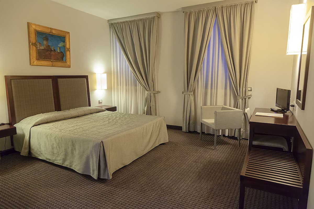 Une chambre d’hôtel avec un lit, un bureau, une chaise, une lampe et un tableau au mur.