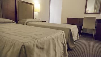 A hotel room with two beds, a desk, a chair, and a lamp.
