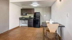 A compact kitchen with a microwave, refrigerator, and dark cabinets. There is a dining table with two chairs and a light fixture above it. - Studio 6 Little Rock, AR - West (Little Rock)