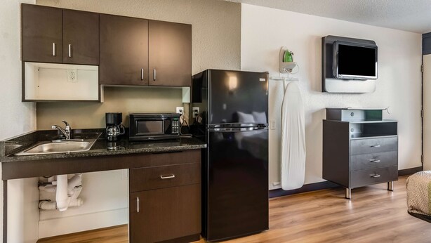 A modern kitchen with dark wooden cabinets, a black refrigerator, a microwave, and a built-in TV. - Studio 6 Little Rock, AR - West (Little Rock)