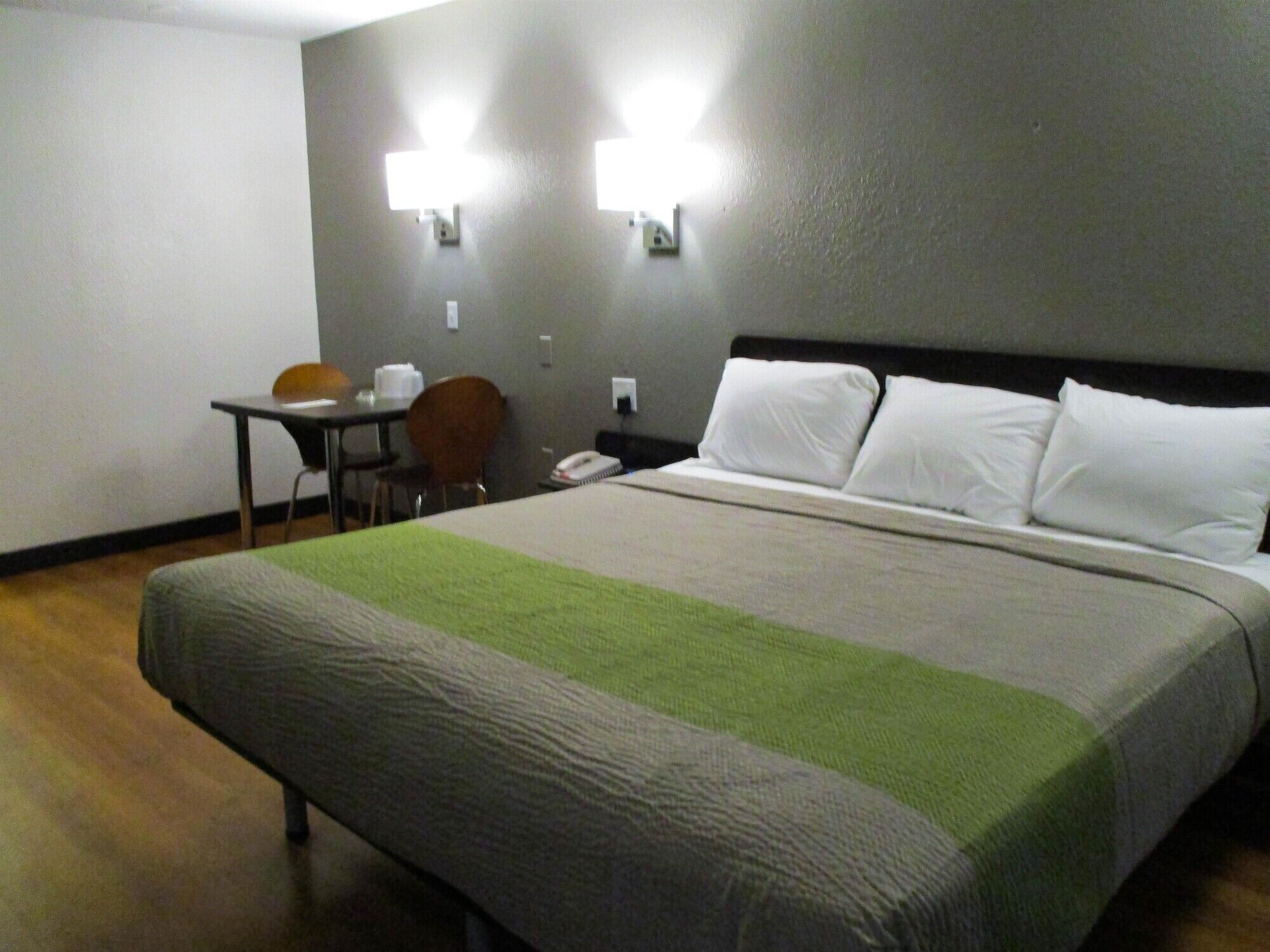 A hotel room with a bed, a desk, a chair, and two wall-mounted lights.