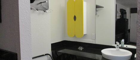 Un baño con un lavabo blanco, un espejo, un perchero para toallas y un armario amarillo.