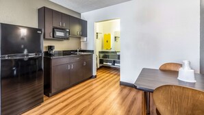 A modern kitchen with dark cabinets, a black refrigerator, a microwave, and a wooden dining table with chairs. - Studio 6 Little Rock, AR - West (Little Rock)