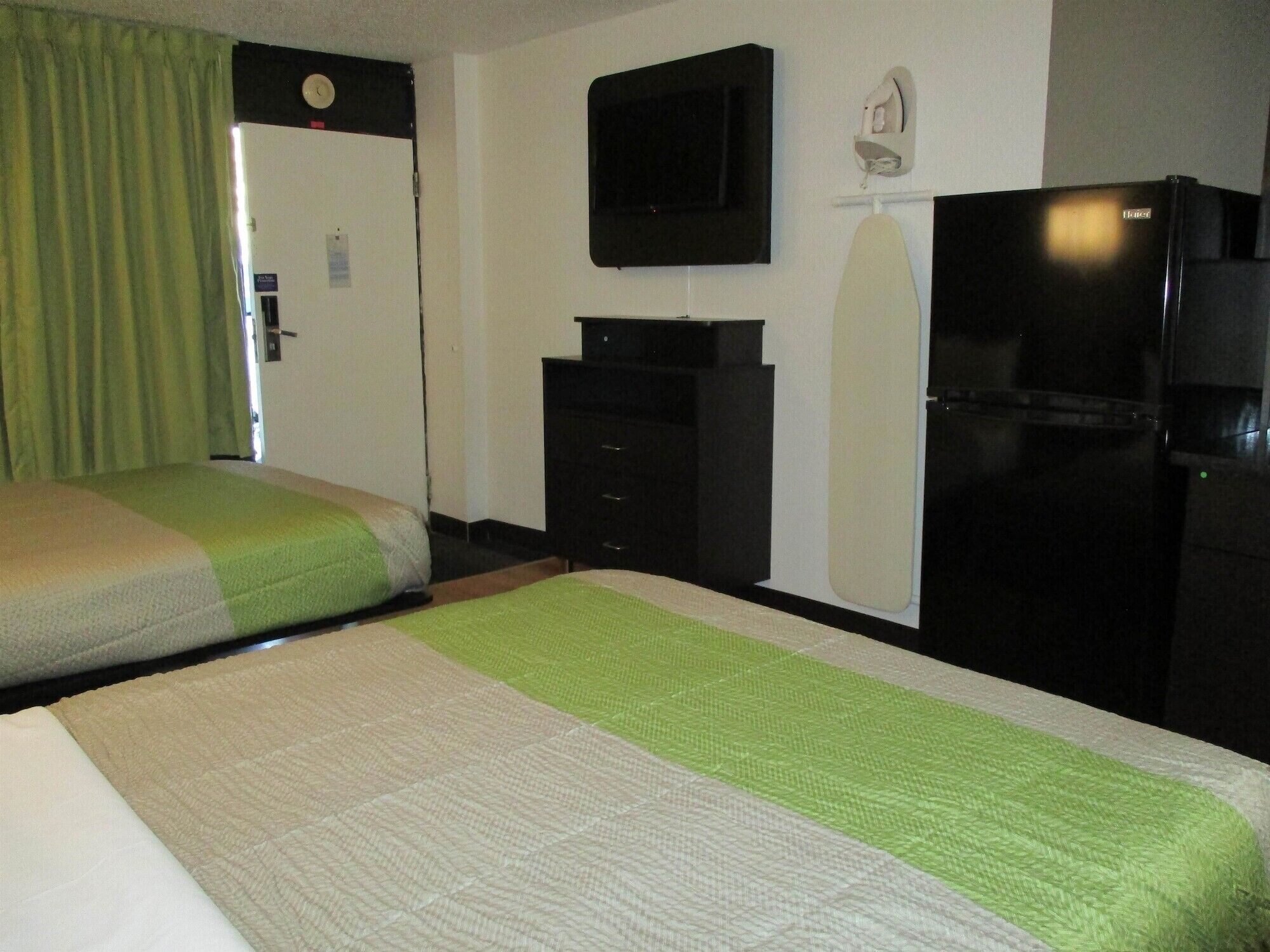 A hotel room with two beds, a television, a refrigerator, and a small desk.