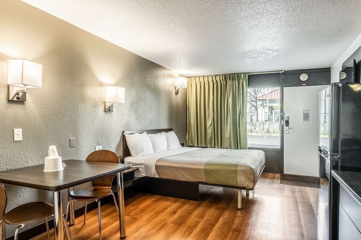 Une chambre d’hôtel équipée d’un lit, d’un bureau, de chaises, d’une table à manger, d’un réfrigérateur et offrant une vue sur l’extérieur.