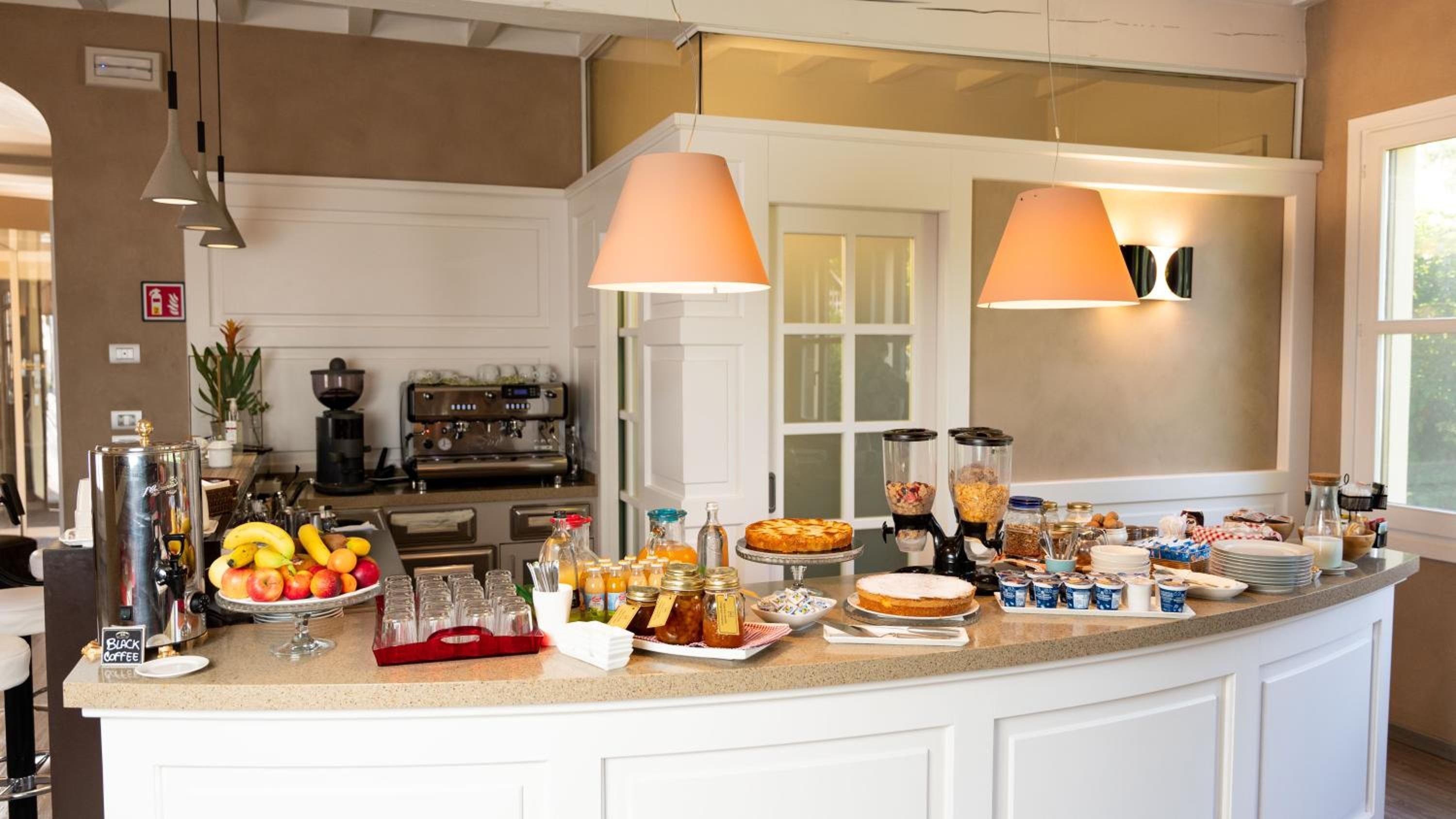 A kitchen with a buffet setup, including fruits, beverages, and a coffee machine.