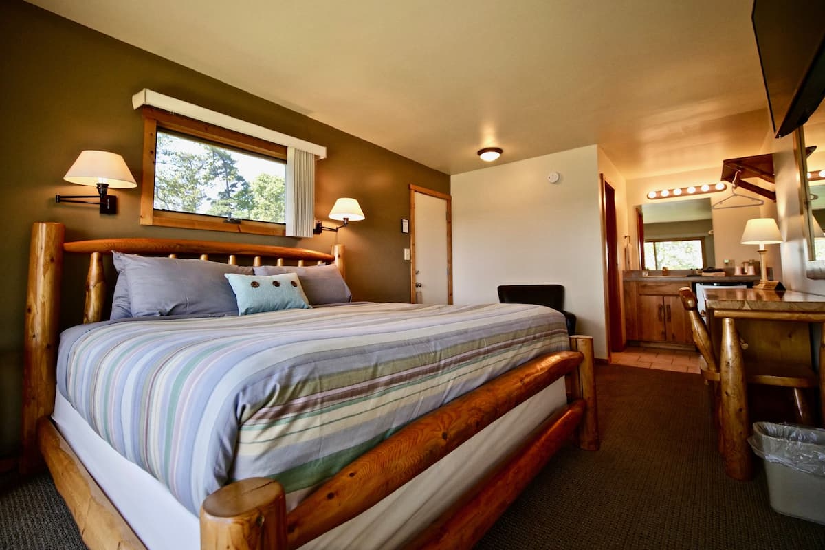 A bedroom with a wooden bed, two bedside lamps, a window, and a mirror above the desk.