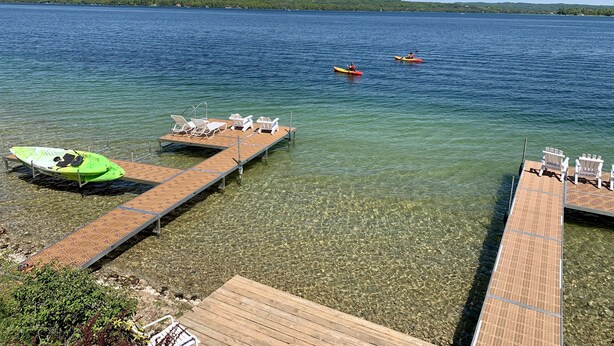 A clear lake with kayaks and a dock with chairs. - Whaleback Inn (Leland)