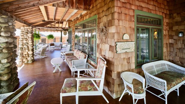 A covered outdoor seating area with wicker furniture and a stone wall.