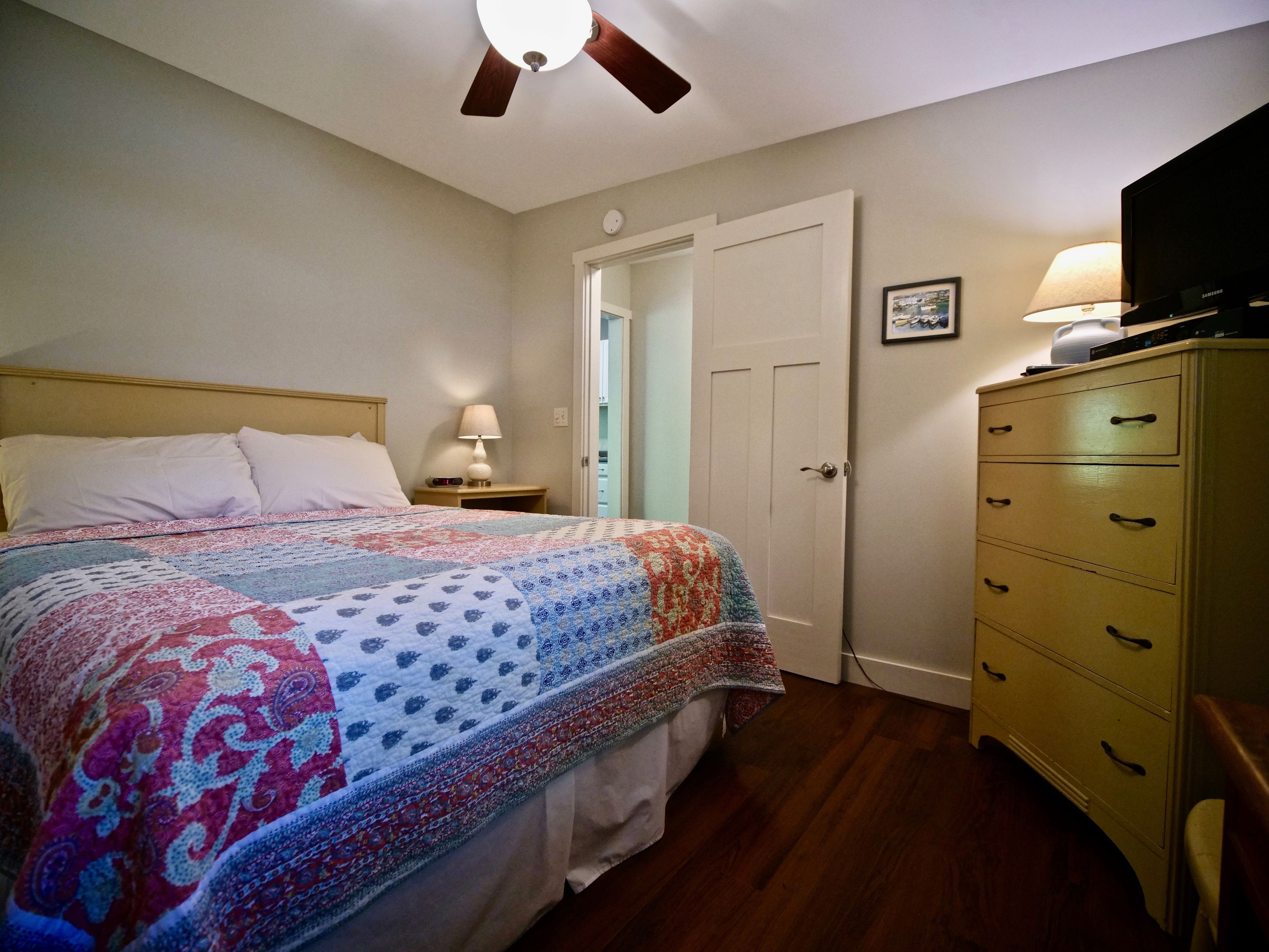A bedroom with a bed, a nightstand, a lamp, a dresser, and a ceiling fan.