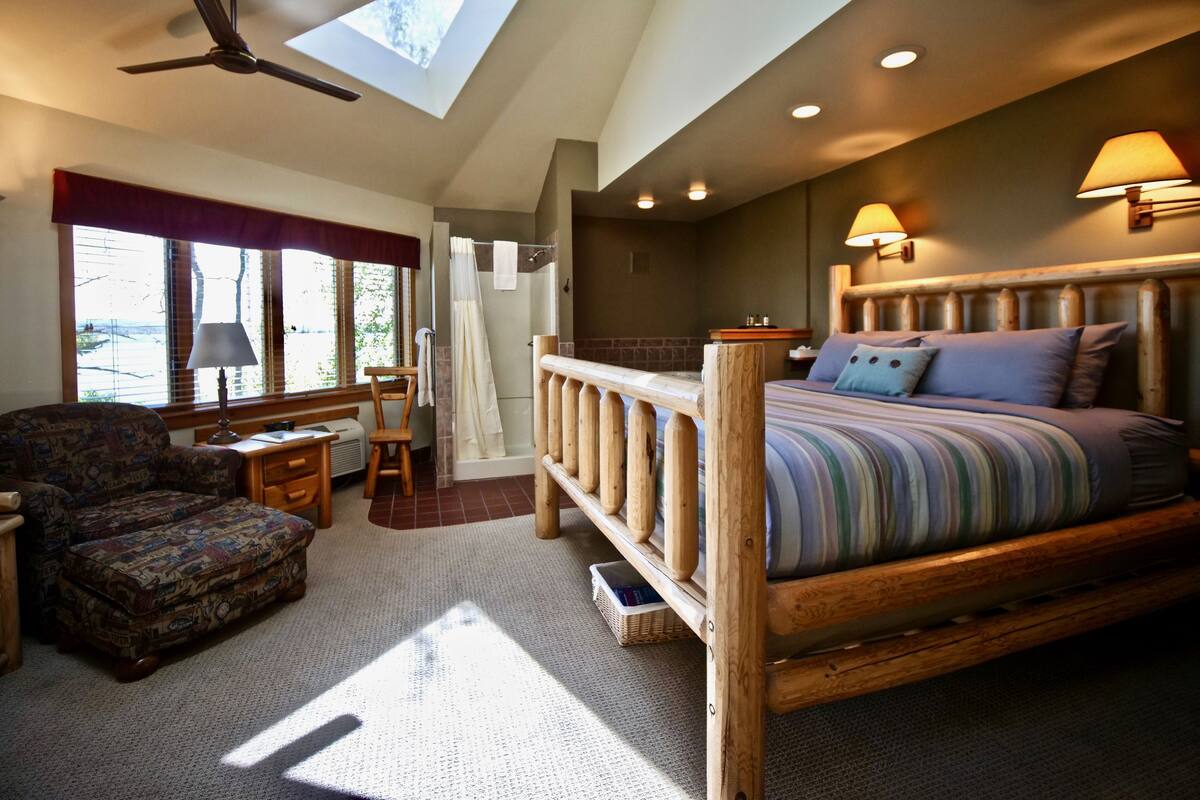 A bedroom with a skylight, a wooden bed, a chair, a desk, and a bathroom with a shower.