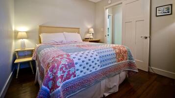A bedroom with a bed, a nightstand, a ceiling fan, a door, and a wall with a picture.