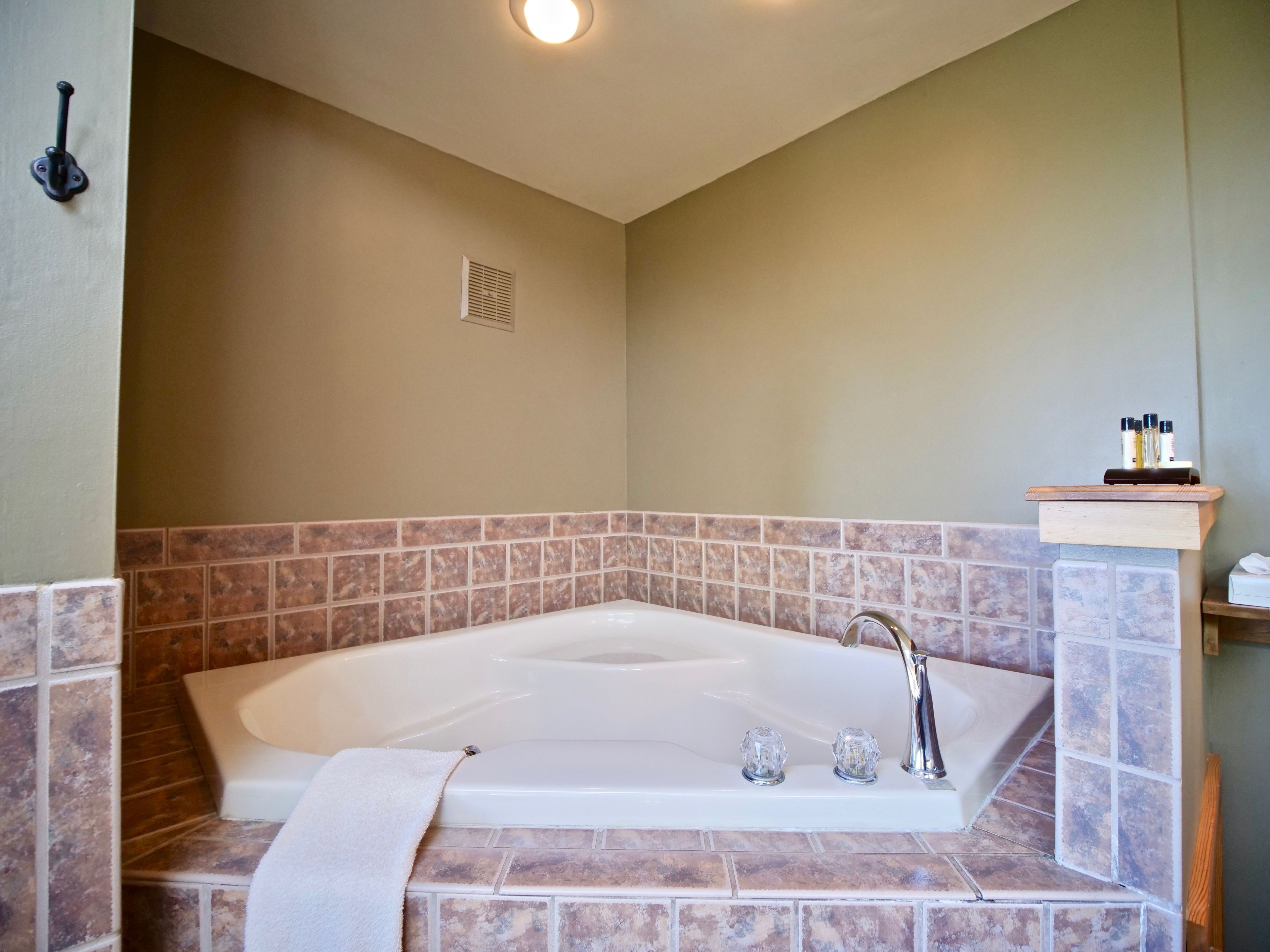 A bathroom with a large bathtub, a towel, and a shelf with toiletries.