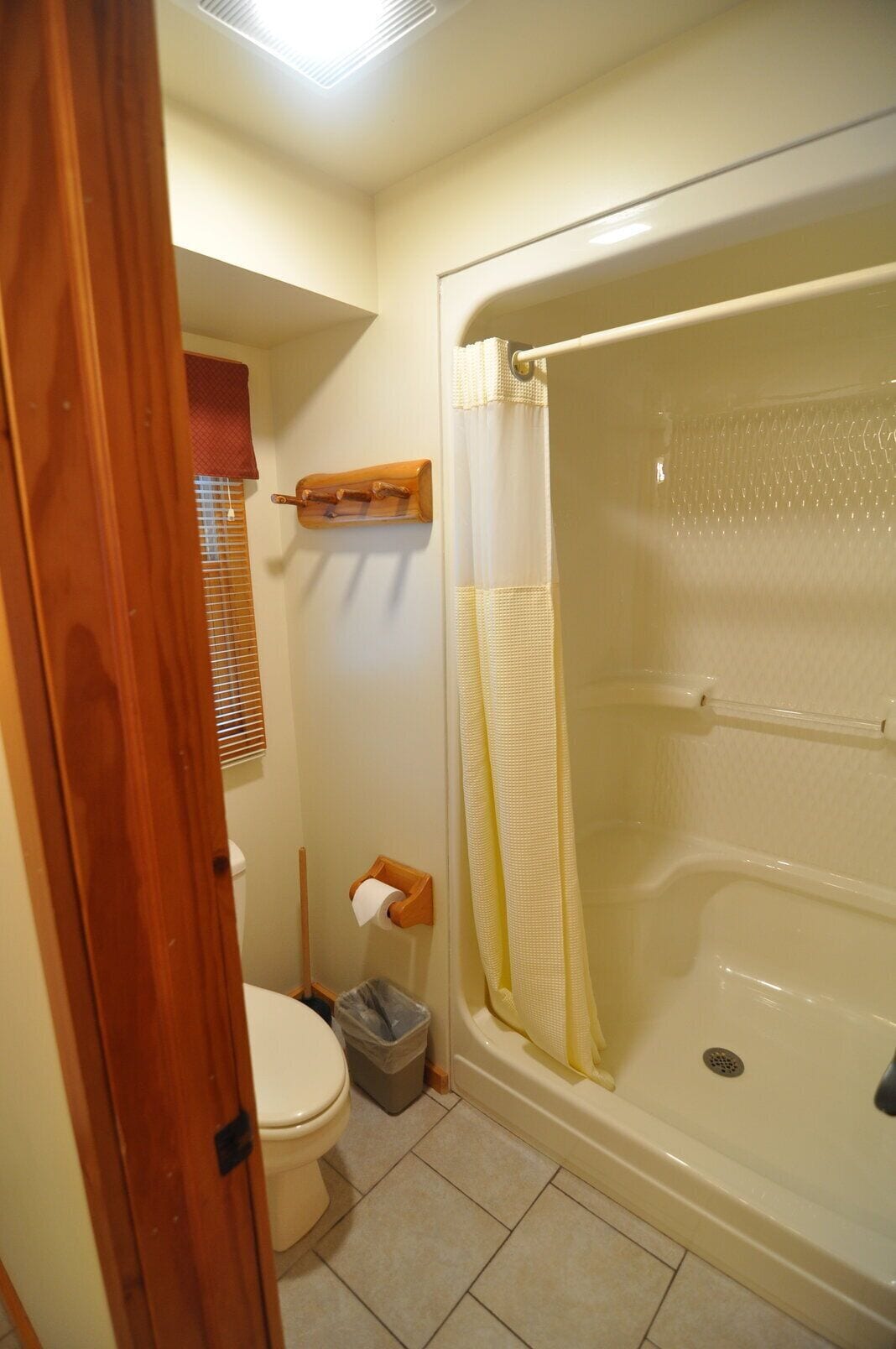 Une salle de bain avec des toilettes, une douche dotée d’un rideau de douche jaune et une étagère en bois au-dessus des toilettes.