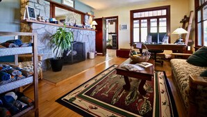 A cozy living room with a stone fireplace, wooden shelves, a large plant, and a patterned rug. - Whaleback Inn (Leland)
