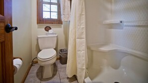 A bathroom with a toilet, a shower curtain, a window with blinds, and a sign on the wall.