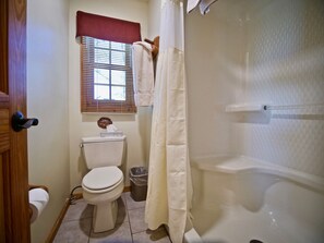 A bathroom with a toilet, a shower curtain, a window with blinds, and a sign on the wall.
