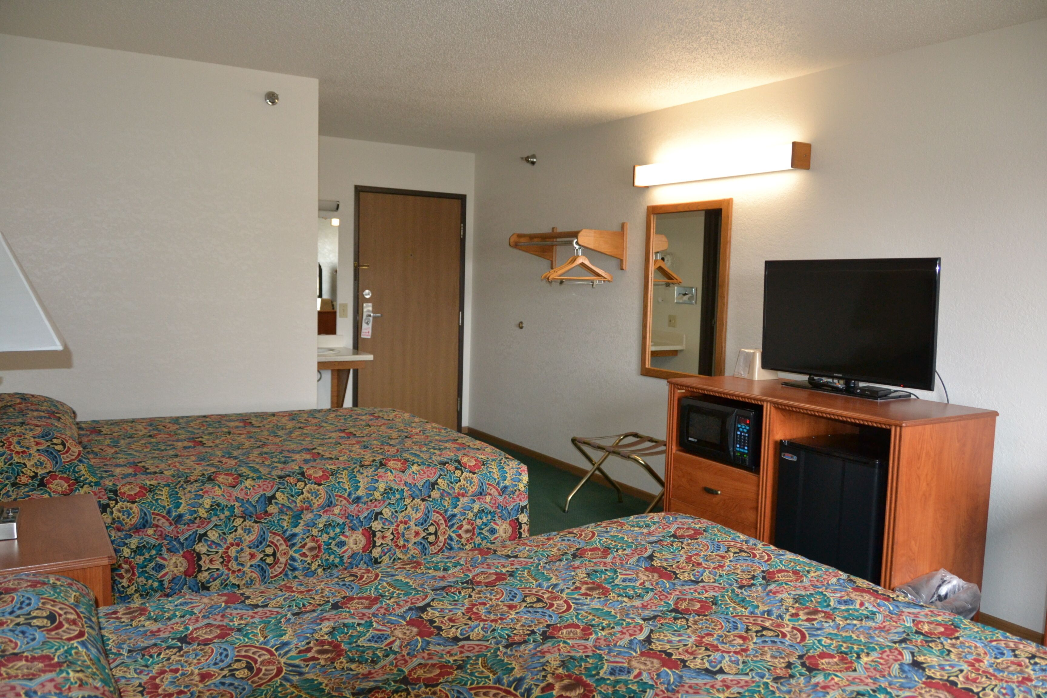 Une chambre d’hôtel avec deux lits, une télévision, un réfrigérateur et une armoire en bois.