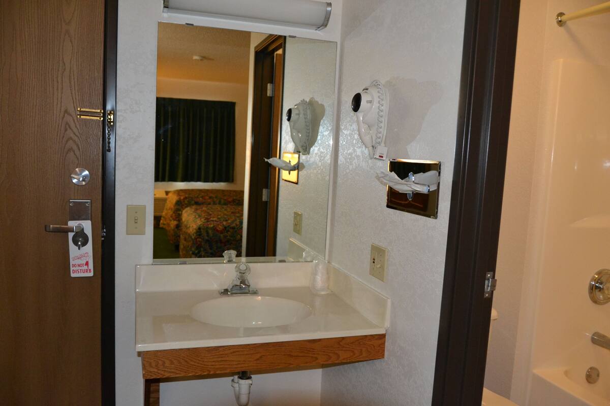 A bathroom with a sink, mirror, towel rack, and a door with a 'DO NOT DISTURB' sign.