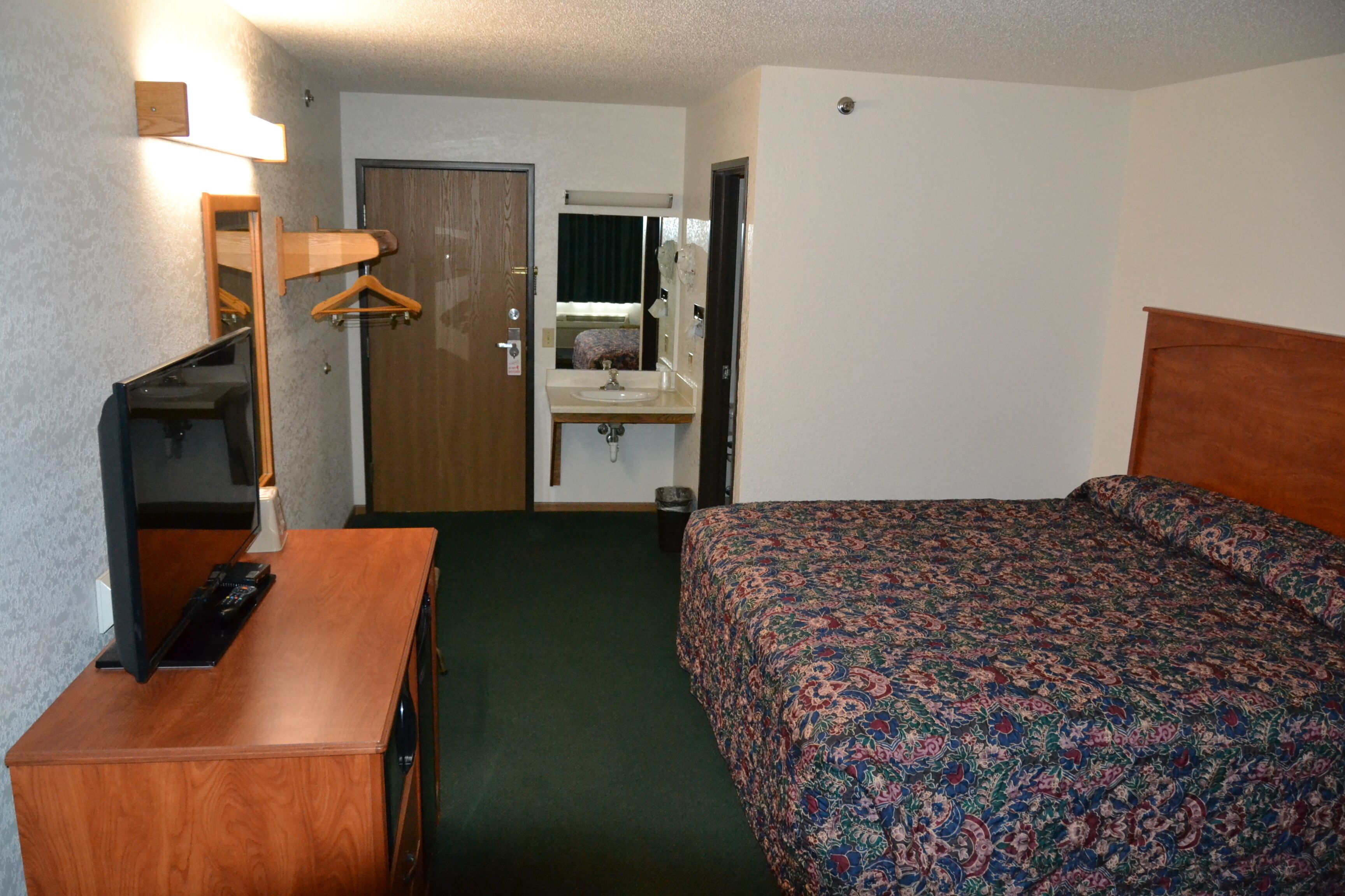 A hotel room with a bed, a desk with a television, a mirror, and a door leading to a bathroom.