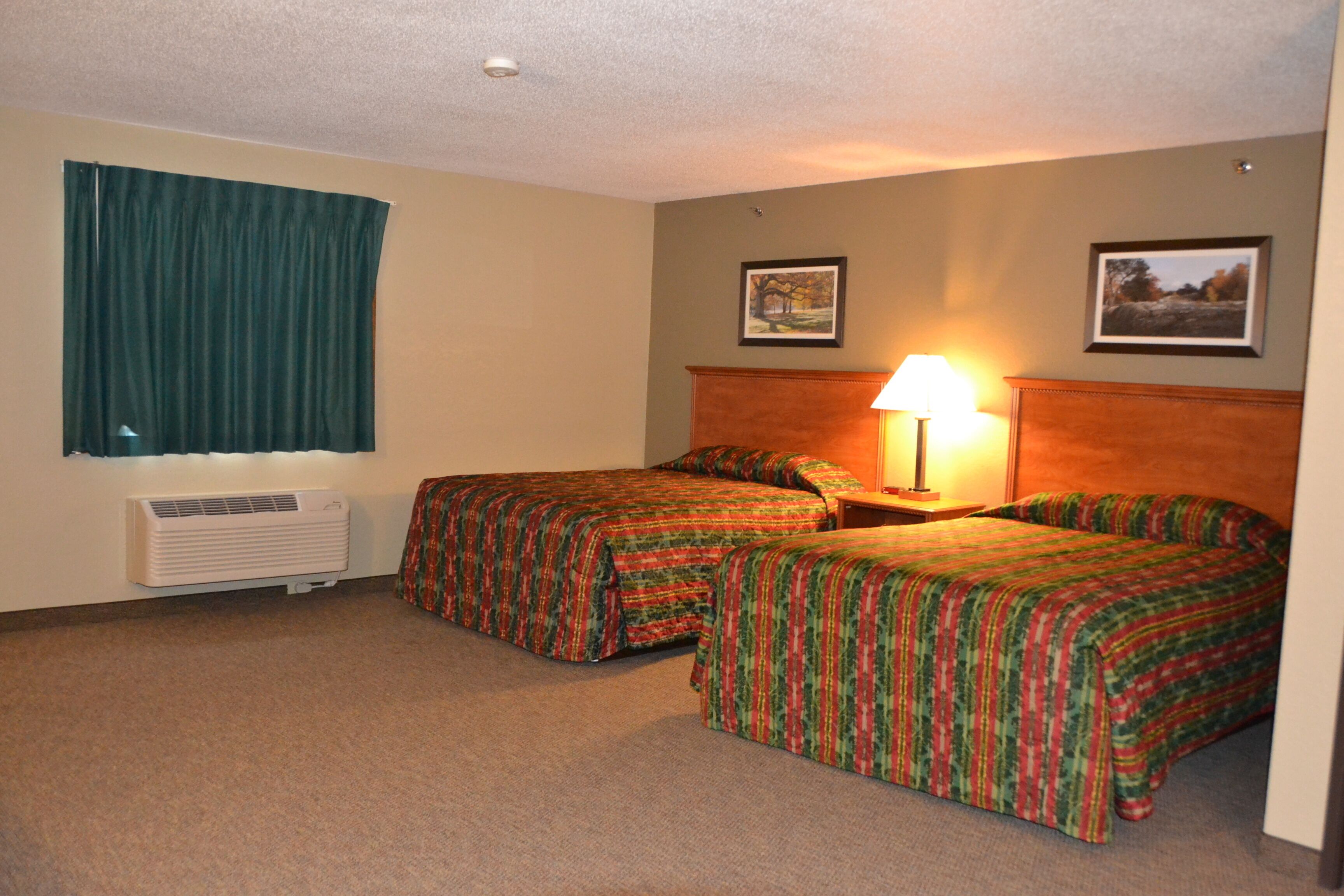 Quarto de hotel com duas camas, uma janela com cortinas, ar condicionado fixado na parede e dois quadros emoldurados.