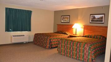 Quarto de hotel com duas camas, uma janela com cortinas, ar condicionado fixado na parede e dois quadros emoldurados.