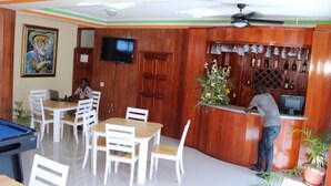 Une pièce aux murs en bois, avec une table de billard, un coin bar avec des bouteilles et un téléviseur.