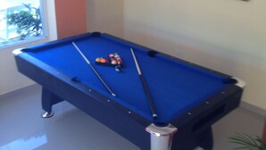 Une table de billard avec des billes et des queues, une fenêtre avec vue et un tableau accroché au mur.