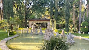 A garden with a circular pond, stone statues, and a building in the background.