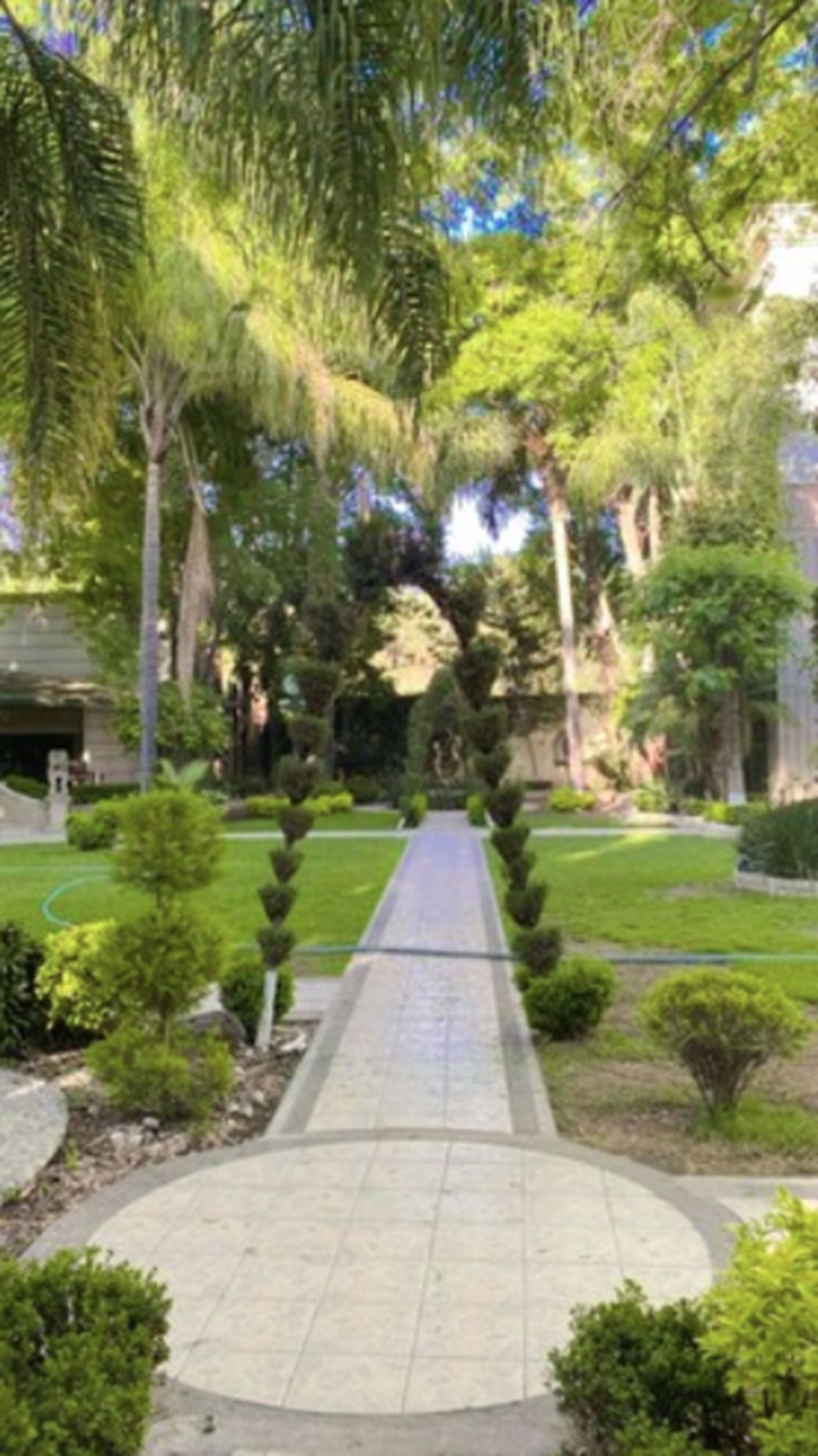 Un sentier qui traverse un jardin bien entretenu, avec des arbustes et des arbres aux formes soigneusement taillées.