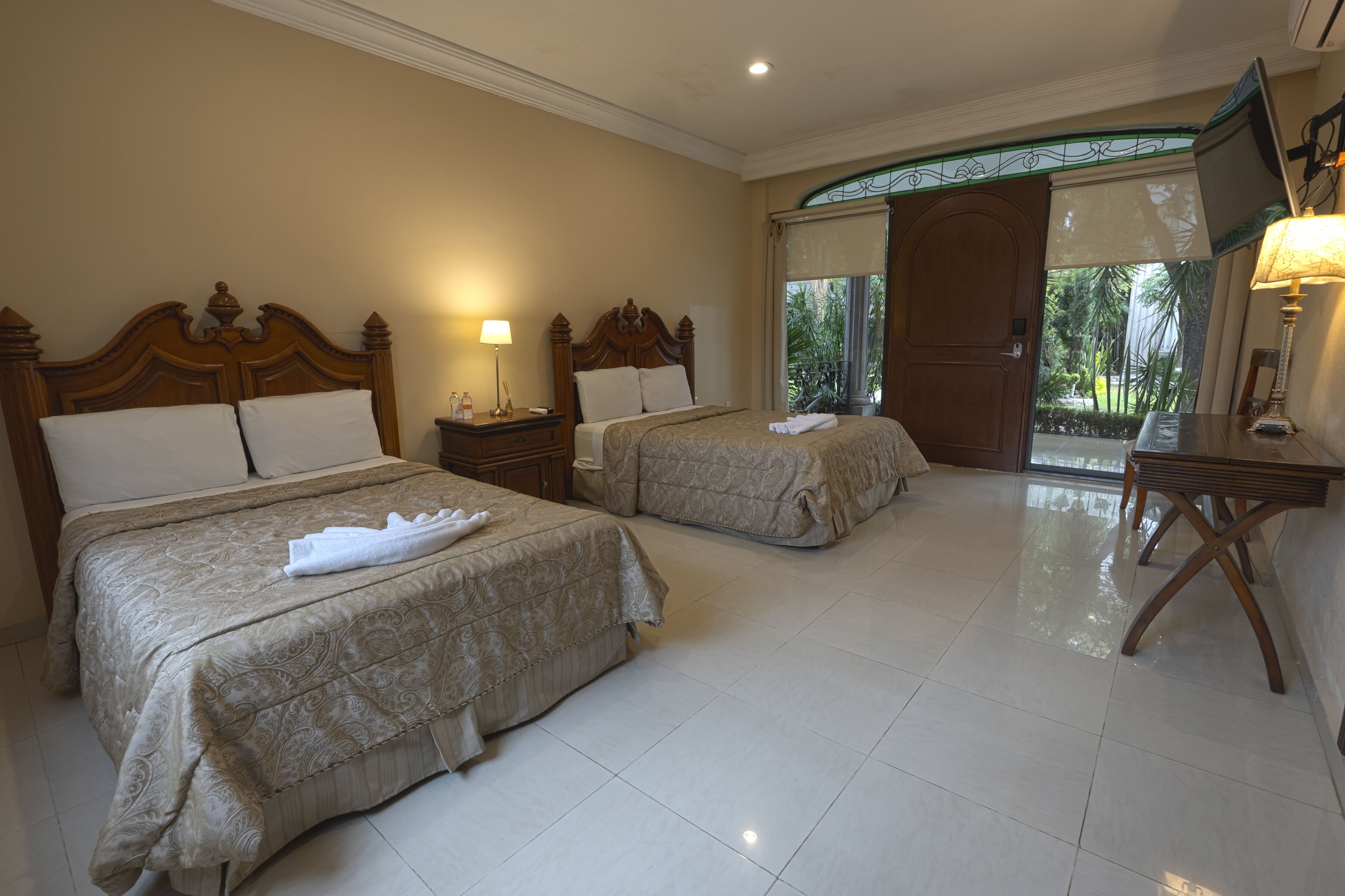 A hotel room with two beds, a TV, and a balcony with a view of palm trees.