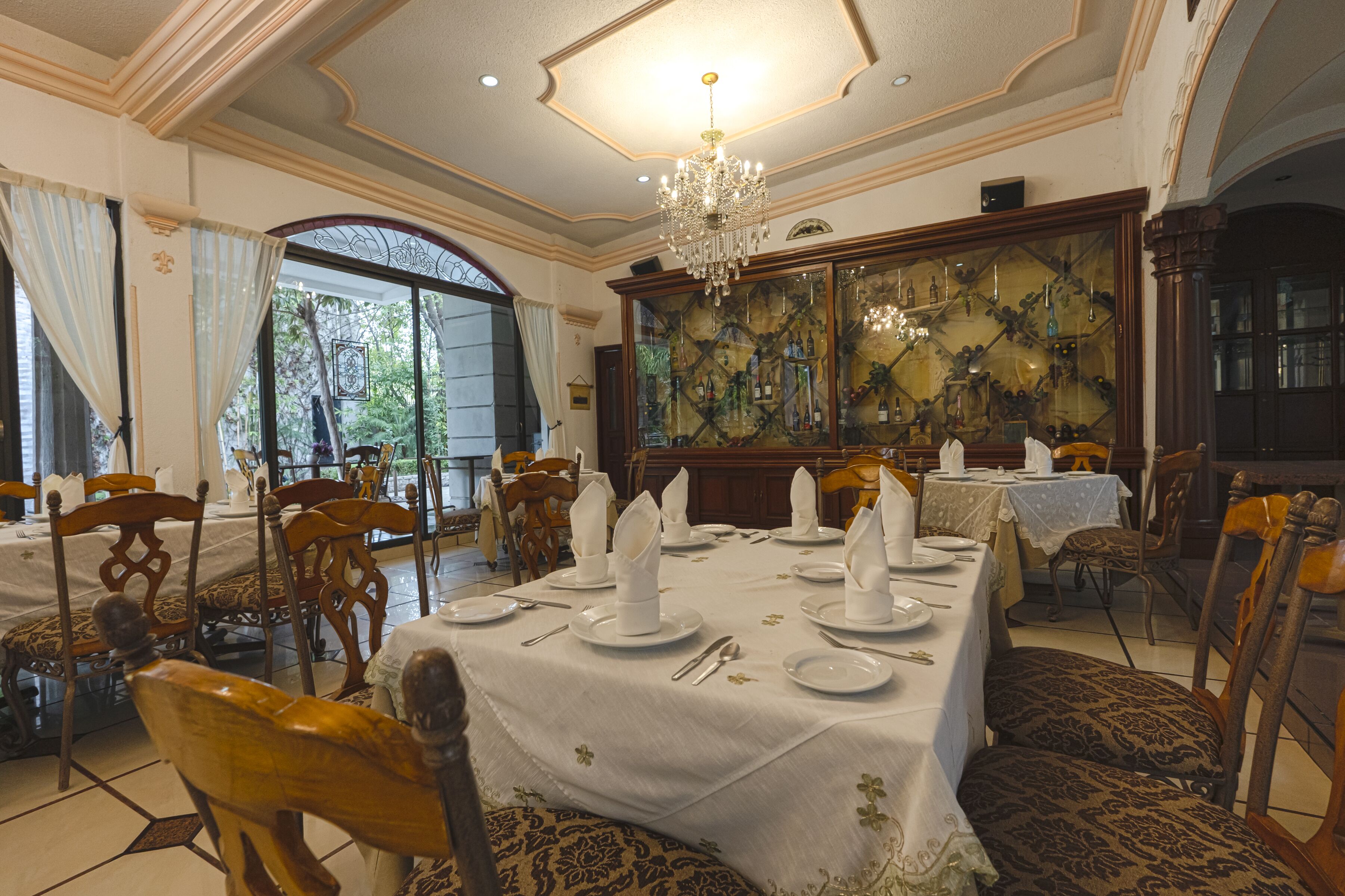 A formal dining room with a chandelier, ornate chairs, and a large window with curtains.