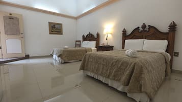 Habitación de hotel con dos camas, una mesita de noche con lámpara, un cuadro enmarcado en la pared y una puerta con placa identificativa.