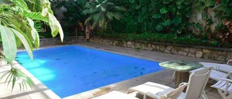 A swimming pool with white lounge chairs and a stone wall with greenery.
