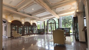 A spacious lobby with a polished tile floor, elegant furniture, and a large arched window offering a view of greenery outside.
