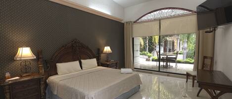 A spacious bedroom with a large bed, two bedside tables with lamps, a flat-screen TV, and a view of a patio with outdoor furniture.