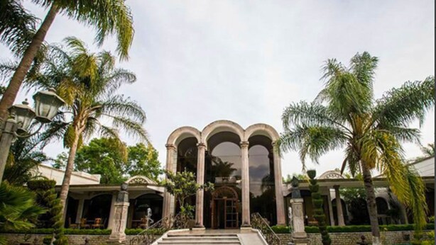 A grand entrance with a central archway, flanked by palm trees and a well-maintained lawn.
