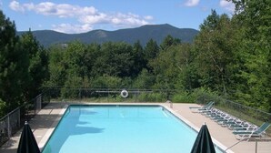 A rectangular pool with a lifeguard chair and a lifebuoy, surrounded by a fence. There are lounge chairs and umbrellas along the poolside. - Sunny Condo w/ Outlet Shops, Expansive Mountain, Valley Views Near North Conway (Intervale)