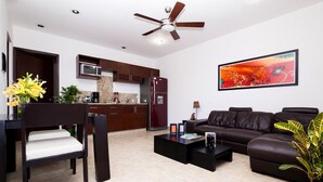 A modern living room with a dark brown leather sofa, a black coffee table, and a dining area with a dark brown chair and a vase of yellow flowers. - Lovely Kingsize-bed Studio, amazing rooftop with pool, best location (unit 203) (Playa del Carmen)